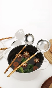 Close-up of stainless steel spoons with natural bamboo handles in a white enamel pot