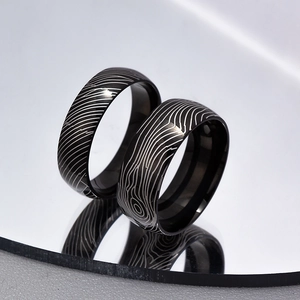 Macro shot of two black titanium rings with Damascus wood grain texture on mirror surface