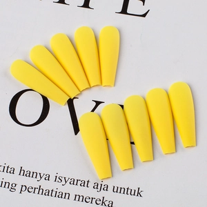 Macro view of bright yellow matte press on nails in long coffin shape displayed on paper