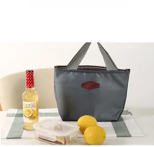Grey insulated lunch bag with woven handle and logo on a checkered tablecloth setting