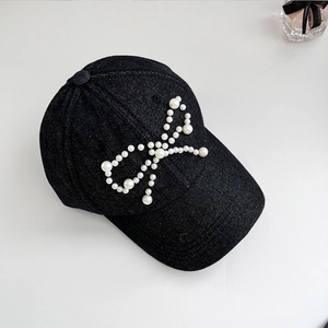 Detail of white pearl bow embellishment on black washed denim baseball cap for women