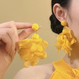 Detail shot of yellow raffia chiffon flower earrings on model and held in hand