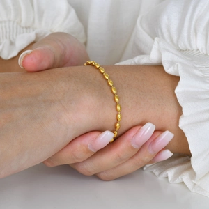 Close-up of a minimalist golden football bead chain bracelet worn on a woman's wrist