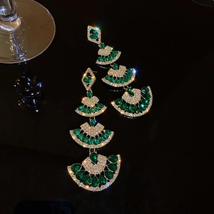Macro shot of fan-shaped drop earrings with green gemstones and sparkling rhinestones