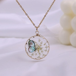 Bohemian gold necklace featuring a round glass pendant with dried flowers and a butterfly