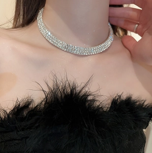 Close-up of triple-row rhinestone choker necklace worn with a black feather top