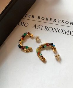Close-up of golden vintage twisted C-shape earrings with colorful stone beads