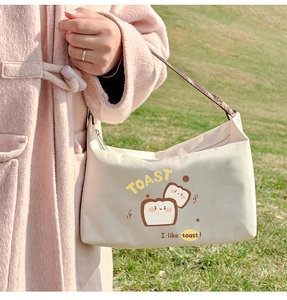 Close-up of beige canvas lunch bag with cartoon toast print held in hand outdoors