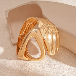 Detail of gold asymmetric hollow geometric bracelet on minimalist cream wavy stand