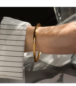 Macro detail of a gold titanium bangle with a single zircon stone on a woman wrist