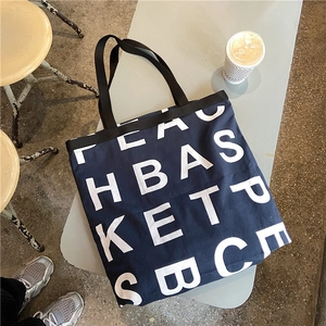 Flat lay of navy blue canvas tote bag with large white letter print on a gray table