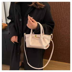Detail of a chic cream pleated dumpling bag featuring a golden bow and crossbody strap