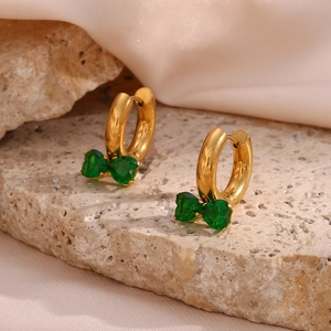 Macro detail of gold bow earrings with green zircon stones on textured natural stone