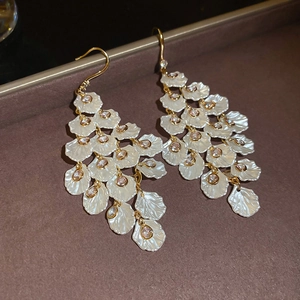 Macro shot of long gold tassel earrings with layered white petal charms and gemstones