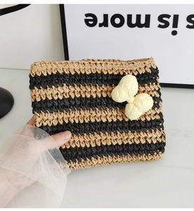 Close-up of a striped straw envelope clutch featuring a beige decorative bow detail