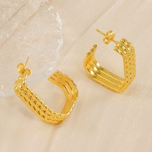 Macro shot of gold-plated twisted rope texture earrings on beige silk background
