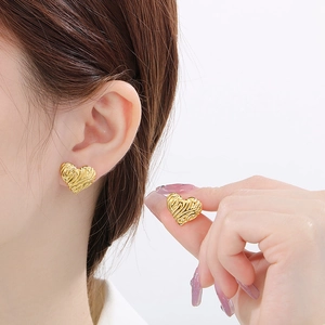 Trendy gold heart stud earrings with irregular wrinkled texture worn by a model