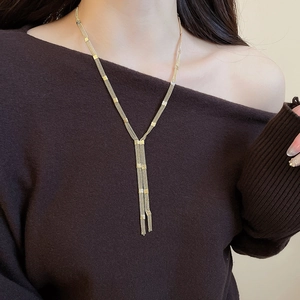 Detail of a golden multi-layer Y-shaped necklace with small square charms on a model