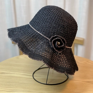 Close-up of black woven sun hat featuring wavy brim and flower detail on a metal stand