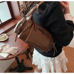 Sac bandoulière en similicuir marron brillant avec plusieurs poches porté par le mannequin