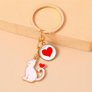 Close-up of golden metal keychain featuring white enamel cat and red heart circle charms