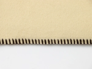 Detailed close-up of beige wool fabric texture with black whipstitch edge detailing