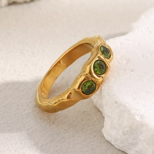 Detail of 18K gold plated stainless steel ring with three green zircons on a white stone