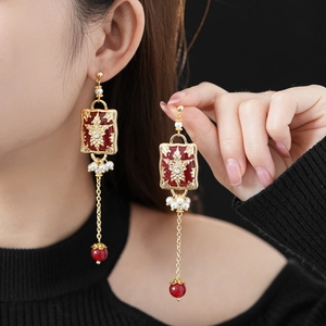 Detailed view of vintage gold earrings with red enamel flowers and pearl fringe on a model
