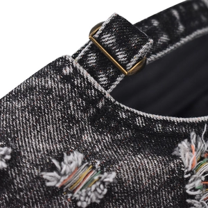 Detailed macro view of distressed black denim fabric with frayed edges and bronze buckle