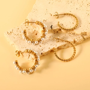 Gold C-shape twist hoop earrings and pearl stud earrings set on a stone display