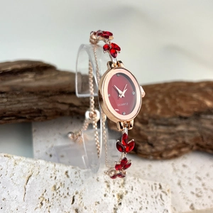 Detail of rose gold oval watch with red gemstone leaf bracelet on natural stone