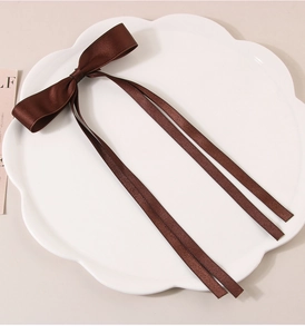 Detail of a brown satin bow hair clip with long ribbons on a white floral ceramic plate