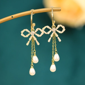 Detail of golden bow drop earrings with sparkling zircon stones and white teardrop pearls