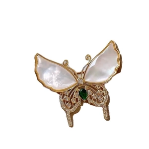 Elegant gold butterfly brooch with white shell wings and a green teardrop stone