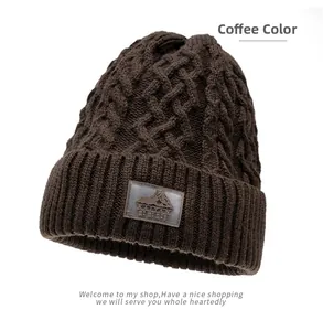 Dettaglio del berretto in maglia a trecce marrone caffè con texture e toppa con logo