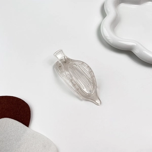 Détail macro d'une pince à cheveux transparente couleur gelée sur fond blanc épuré