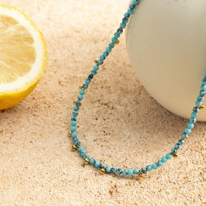 Detail of 18K gold plated stainless steel necklace with blue turquoise beads on stone surface