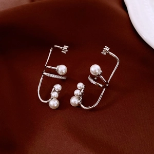 Close-up of silver ear cuff with zircon stones and pearls on dark fabric background