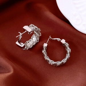 Detail of silver-plated hoop earrings with woven texture on red silk background