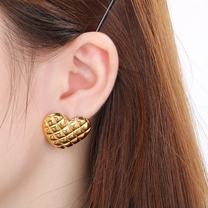 Close-up of heart-shaped gold stud earring with quilted pattern on a woman's ear