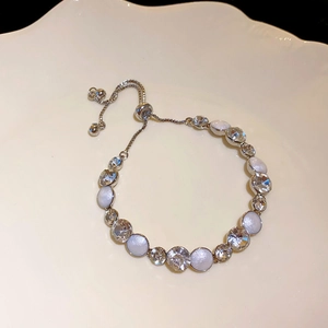 Detail of silver bracelet with white cat eye stones and round crystals on a ceramic plate