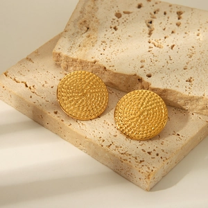 Détail de boucles d'oreilles rondes dorées avec texture tissée sur pierre naturelle