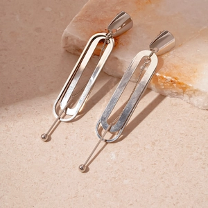 Detail of silver geometric earrings with oval chain links on white marble stone