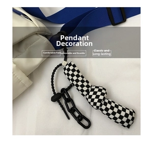 Detail of checkered cloth pendant with black plastic chain on white quilted messenger bag
