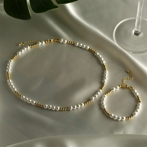 Elegant pearl and gold bead necklace and bracelet set on silk fabric with green leaves