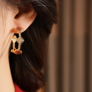 Macro view of gold-plated clover earrings with beaded edge worn by a model