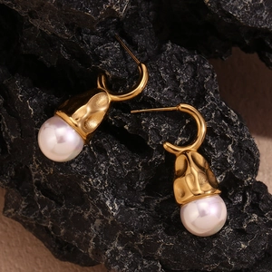 Detailed view of 18K gold hammered metal texture and white pearl drop earrings on dark rock