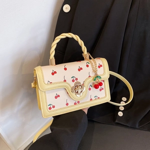 Women's cherry print crossbody bag with yellow trim and flower lock held by hand