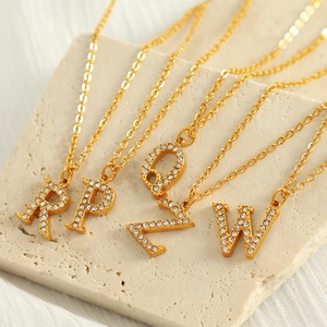 Elegant gold titanium steel alphabet necklaces with crystals on a beige stone slab
