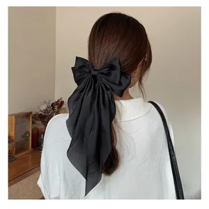 Elegant large black satin bow hair clip with long ribbons worn by a model in home setting